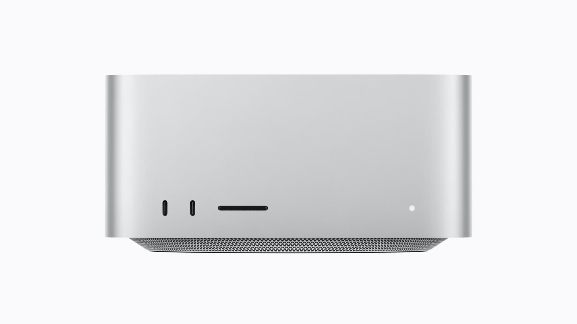 A silver Mac Studio seen head-on against a light gray background, with two USB-C ports, an SD card slot and a small white power light on its front face above a perforated base.
